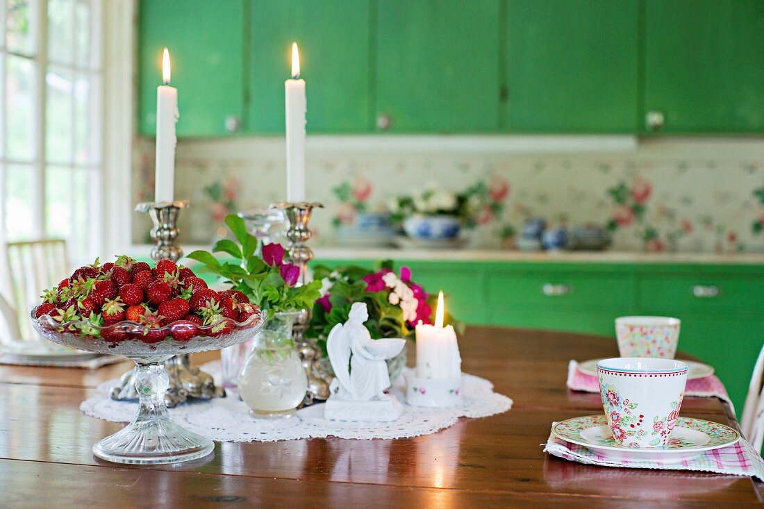 Gedeckter Tisch mit frischen Erdbeeren, Blumen und brennenden Kerzen