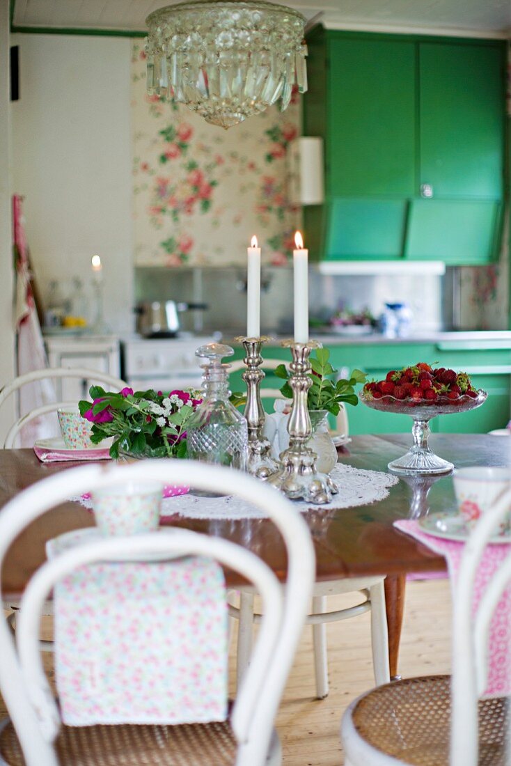 weiße Thonetstühle um Tisch, darauf Silber Kerzenhalter mit brennenden Kerzen und frische Erdbeeren in Schale