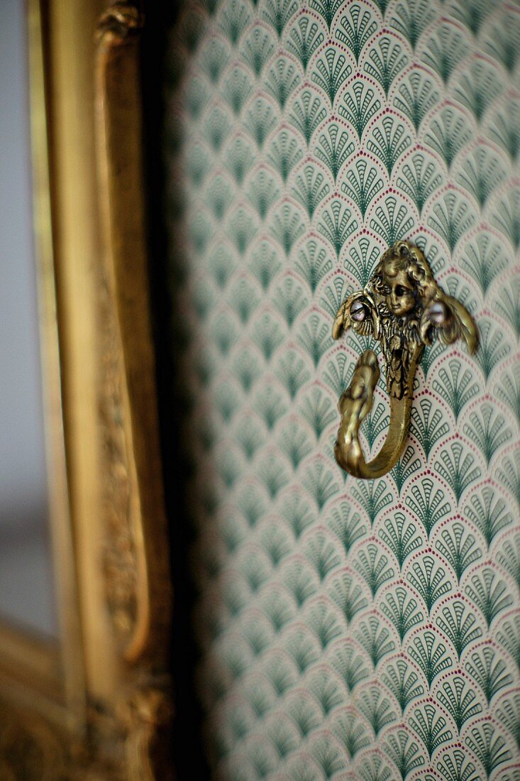 Brass hook on wall with ornately patterned wallpaper