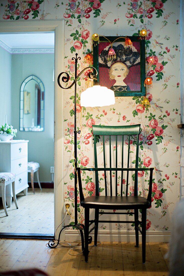 Grüner Holzstuhl und Vintage Stehleuchte mit hellem Schirm vor tapezierter Wand mit Blumenmuster, seitlich offene Tür