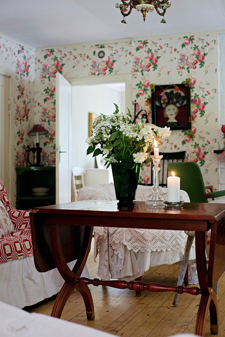 Weisser Blumenstrauss in Vase auf antikem Holztisch, in ländlichem Wohnzimmer mit Blumentapete an Wand