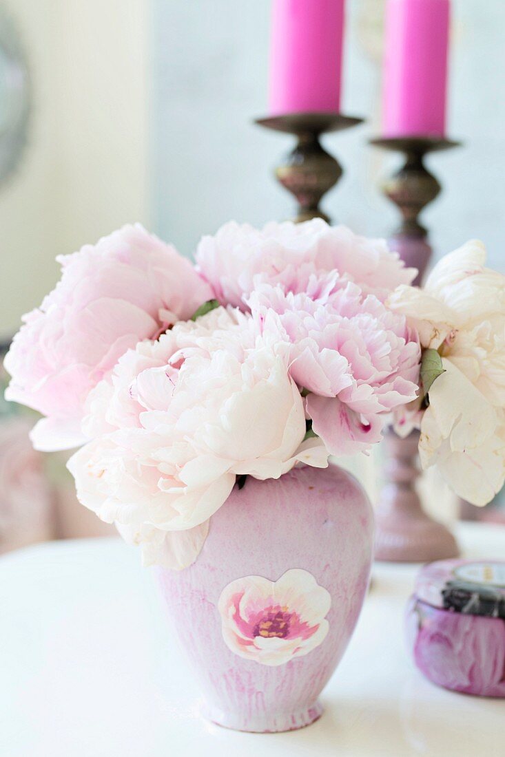 Rosa Vase mit Pfingstrosen vor Kerzenhaltern mit pinkfarbenen Kerzen