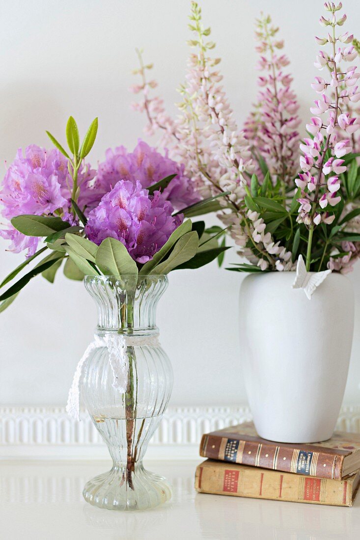 Vases of flowers and books on white surface