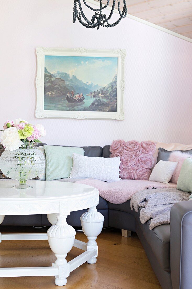 Weisser Couchtisch vor grauer Eckcouch mit Kissen, an pastellrosa Wand mit Landschaftsbild