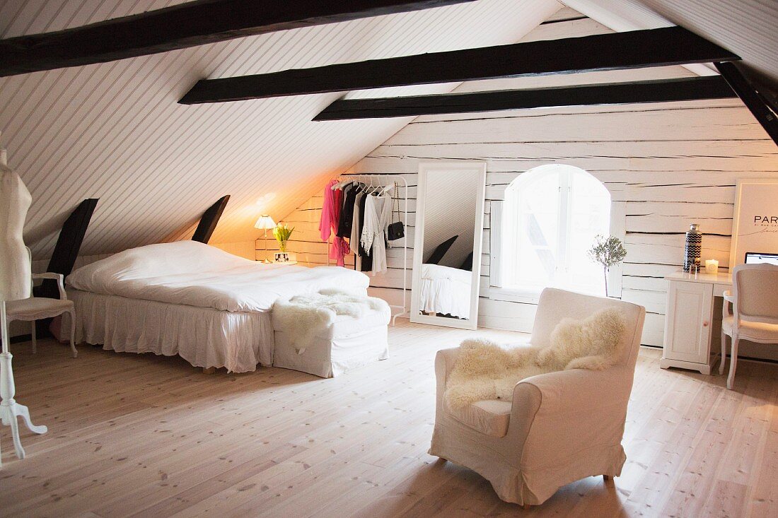 Feminines, weisses Schlafzimmer in ausgebautem Dachstuhl mit dunklen Holzbalken