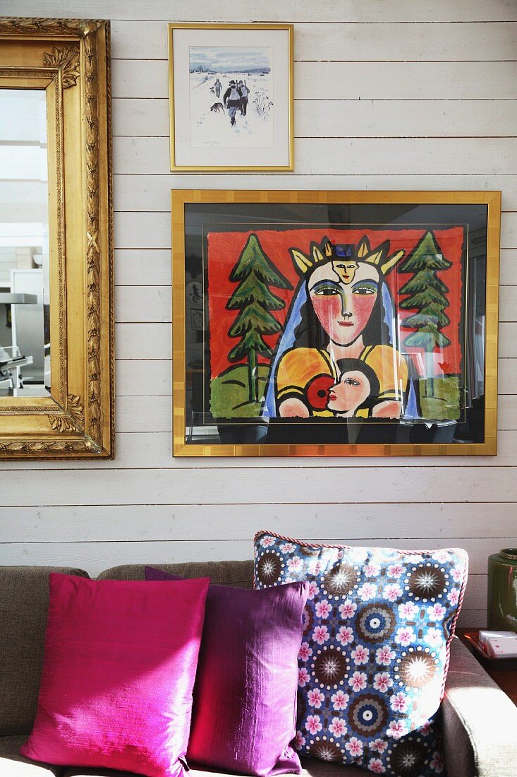 Modernes Bild und goldgerahmter Spiegel auf holzverschalter Wand; Dekokissen - floral und unifarbig auf Sofa
