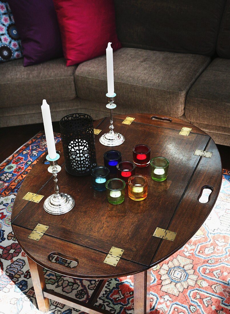 Tealights in colourful glasses and candlesticks on traditional wooden table
