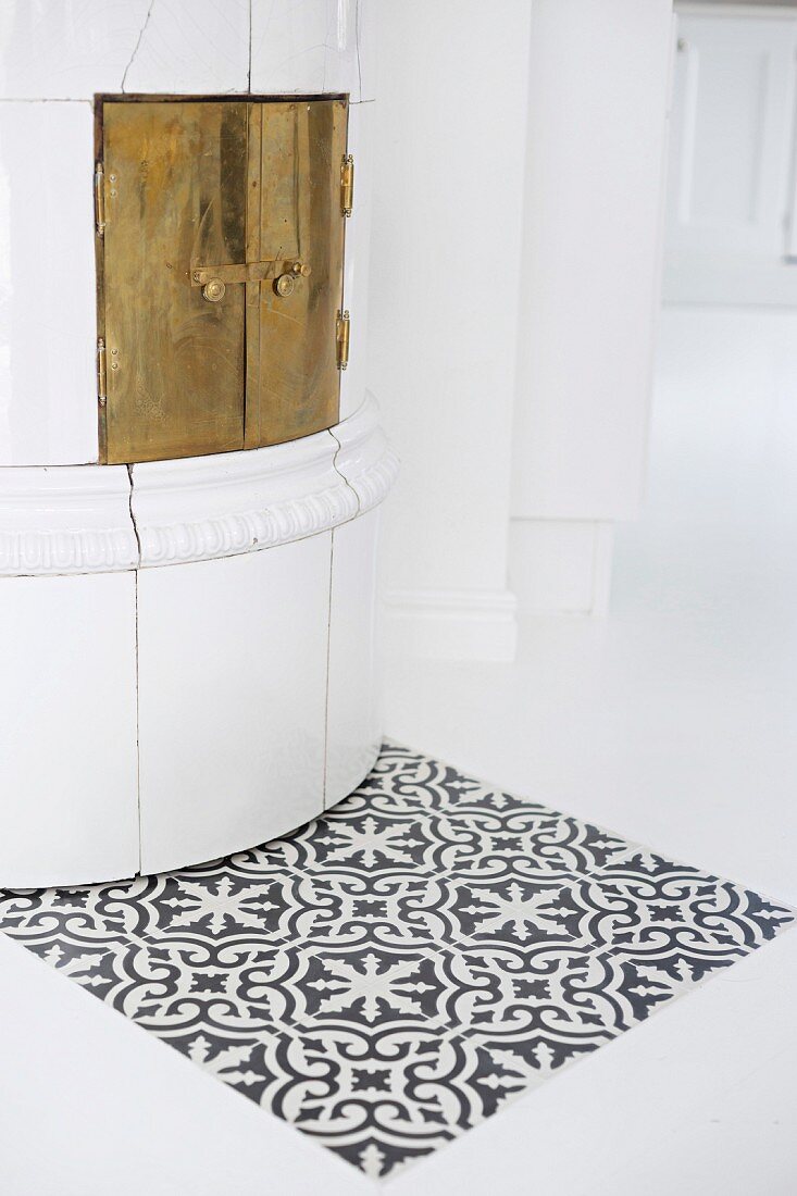 Patch of tiles with Oriental pattern in front of traditional tiles stove with brass door in white, purist interior