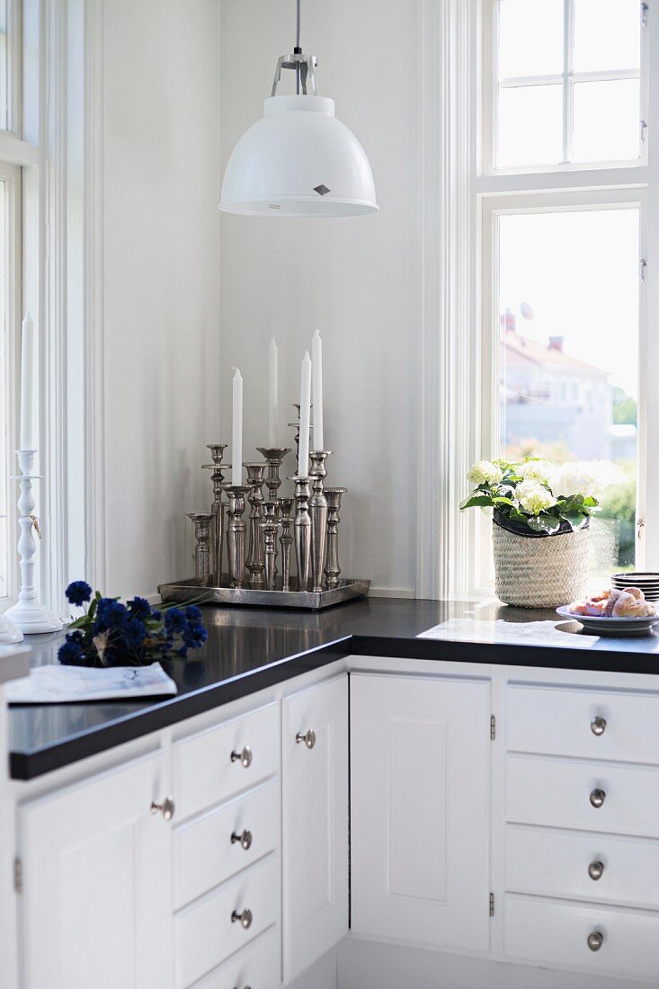 Silver candlesticks on L-shaped kitchen base units below retro pendant lamp