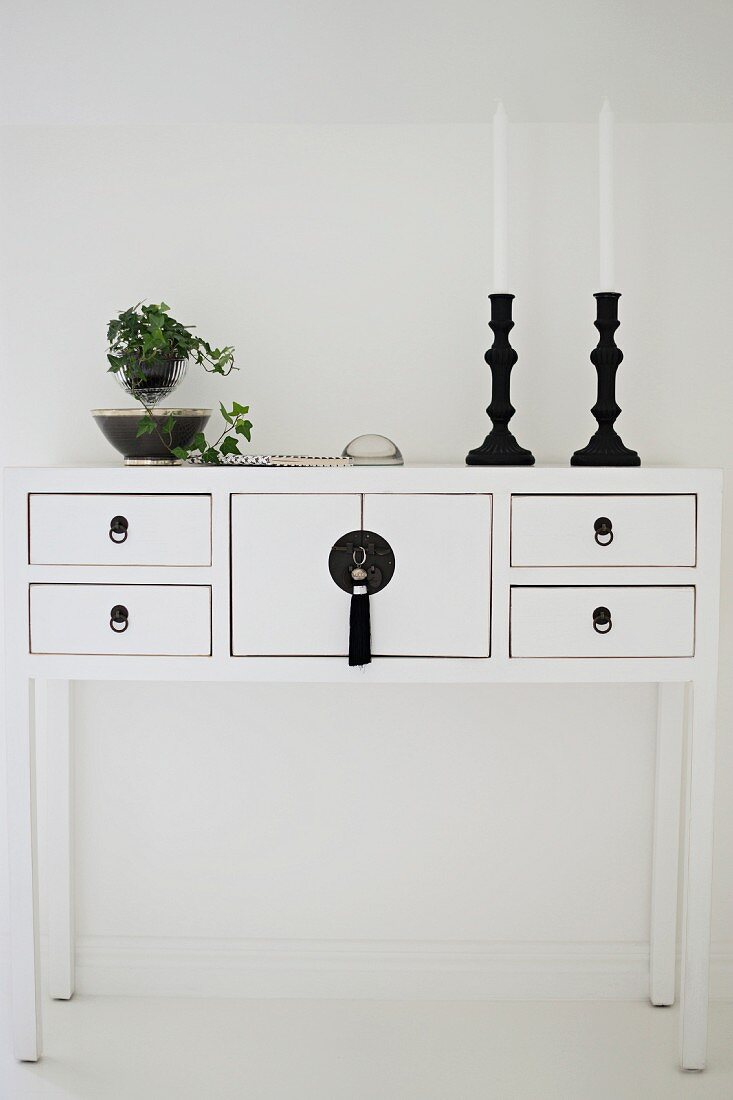 Black candlesticks and ivy on white lowboy cabinet against wall