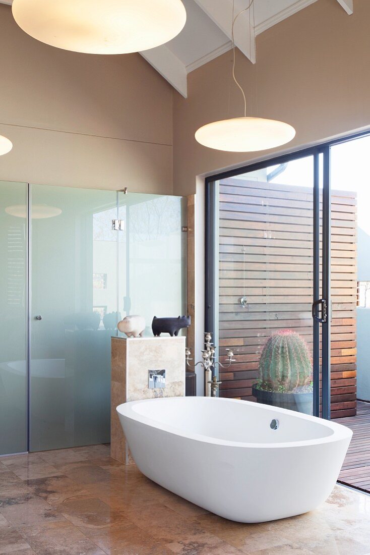 Free-standing bathtub on elegant tiled floor next to terrace doors and shower screen