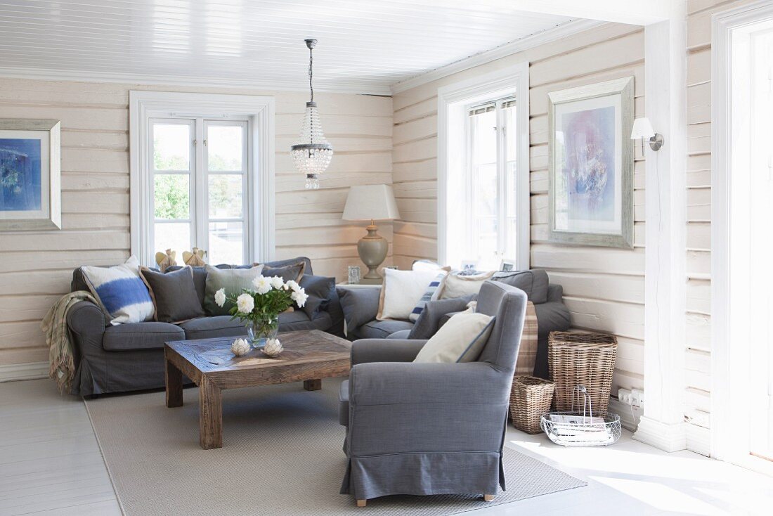 Grauer Sessel und Sofa um rustikalem Holz Couchtisch in holzverkleideter Wohnzimmerecke