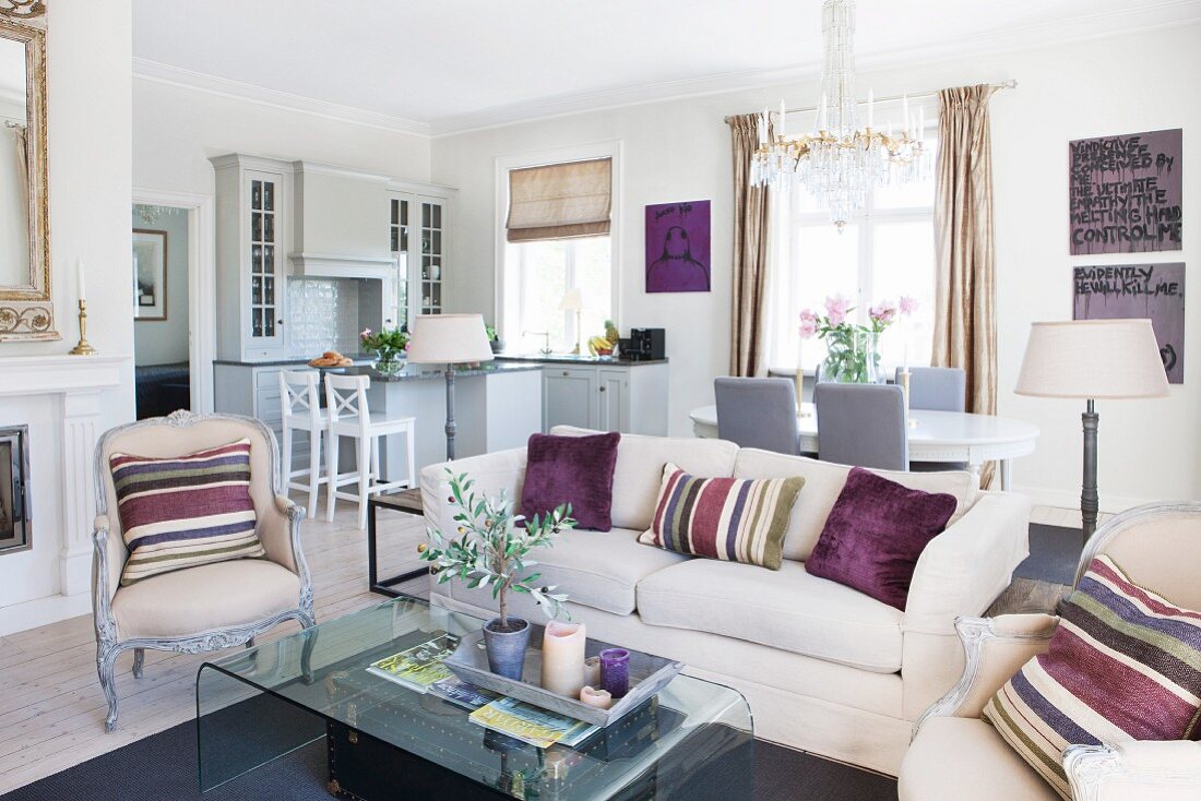 Loungebereich mit hellem Sofa und Sessel im Rokoko-Stil, dekoriert mit gestreiften Kissen, in offenem Wohnraum