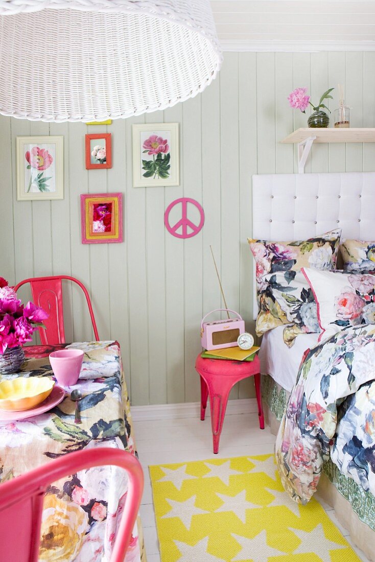 Bett und Tisch auf engem Raum mit blumigen Textilien, pinkfarbenen Retrostühlen und Accessoires