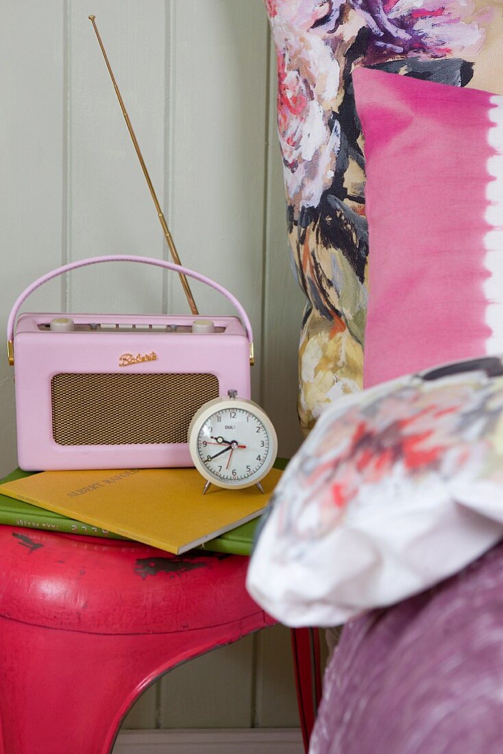 Rosa Retro Radio und Wecker auf pinkfarbenem Vintage Hocker und grossblumiger Bettbezug