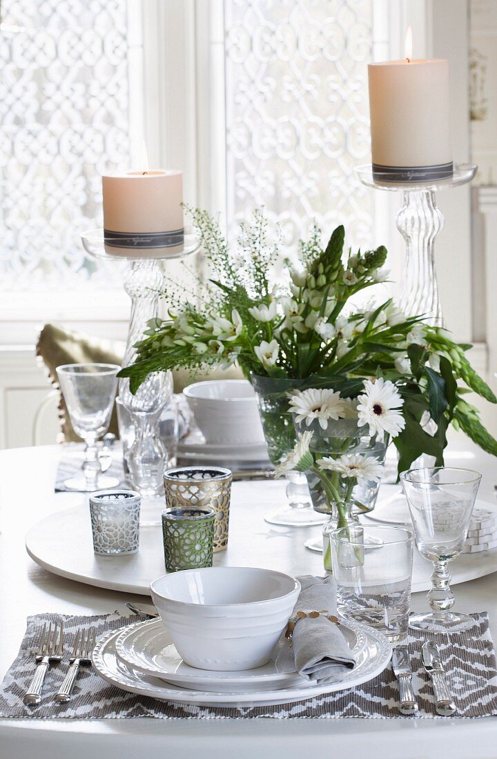 Gedeck mit weissen Tellern und gemustertem Platzset, auf Tisch drehbare Platte mit Windlichtern und Blumenvasen