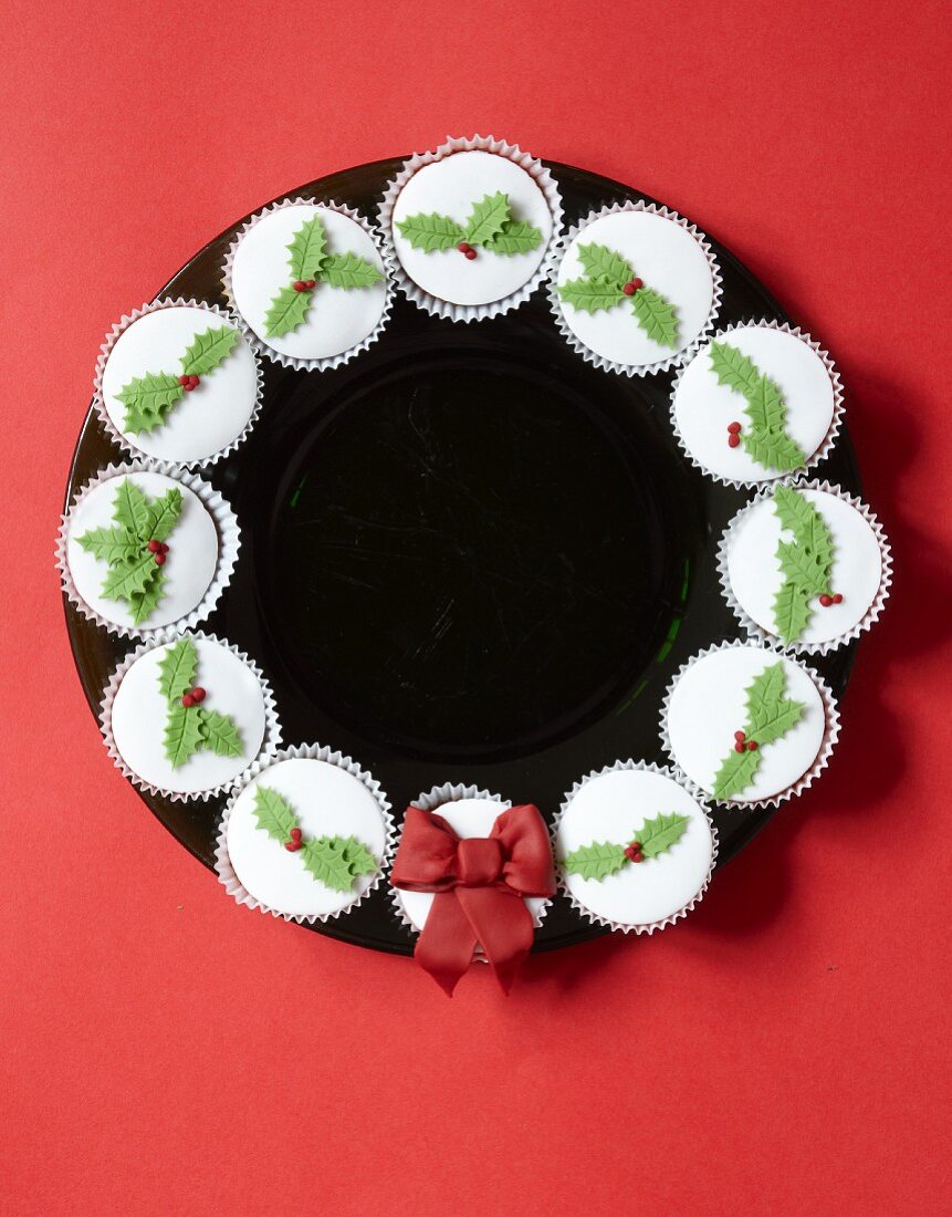 Kranz aus weihnachtlich verzierten Cupcakes auf schwarzem Teller