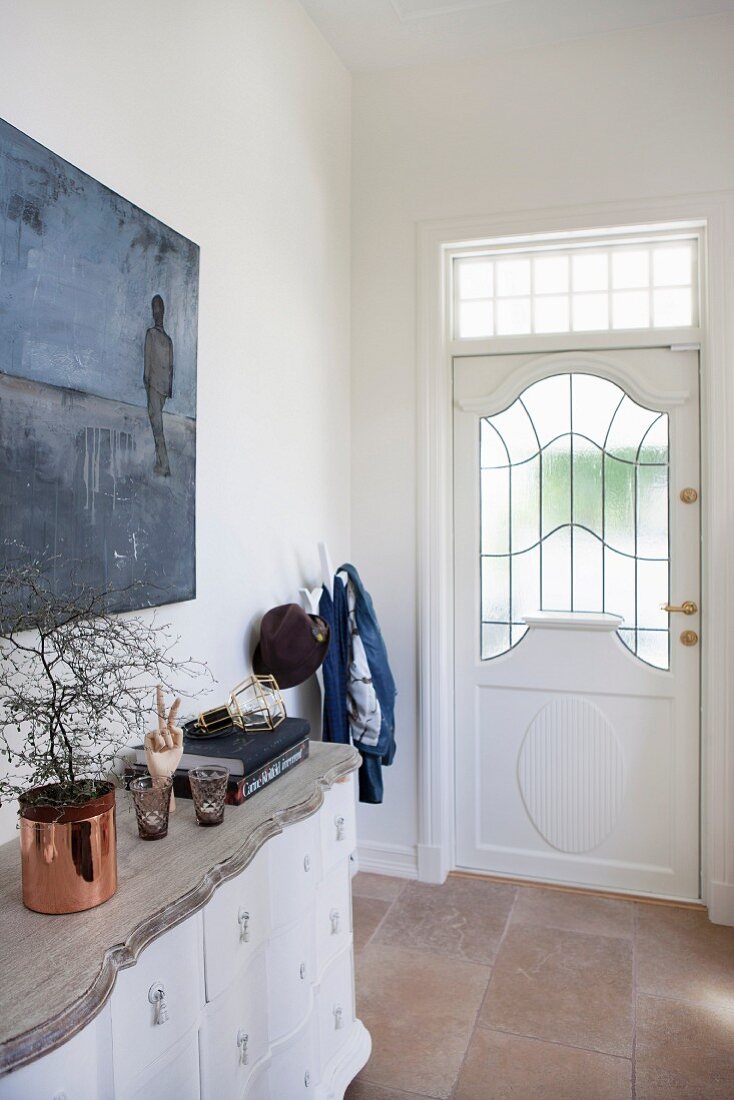 Kommode mit geschnitzter Holzplatte, vor Wand mit Bild im Hauseingang, Haustür mit Glasfüllung und Oberlicht