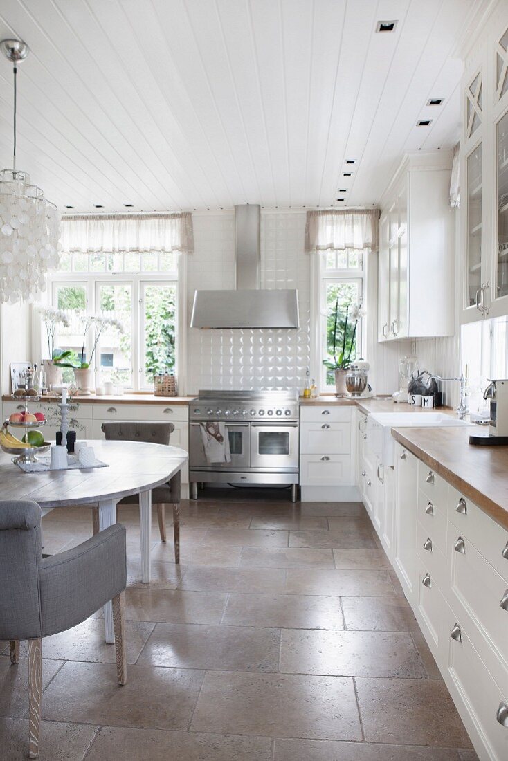 Essplatz mit Polsterstuhl in weisser Landhausküche, mit grossformatigen Steinbodenfliesen