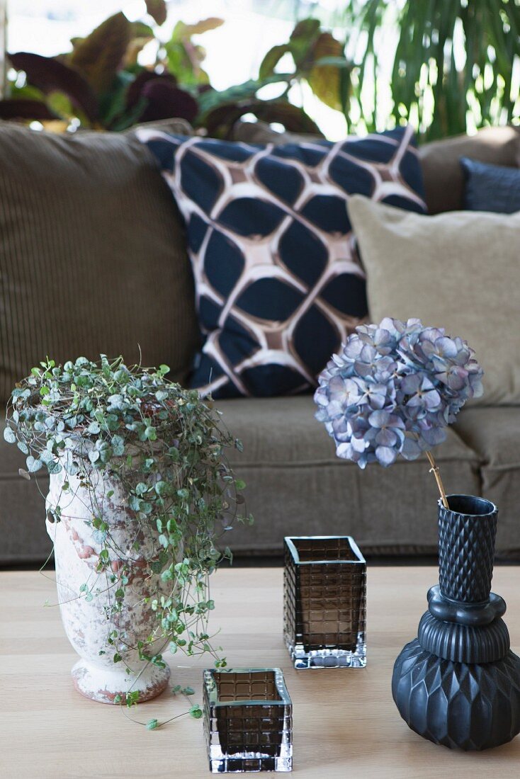 Grünpflanze im Vintage Blumentopf, Hortensie in Vase und Windlichter auf Tisch, gegenüber Sofa mit Kissen