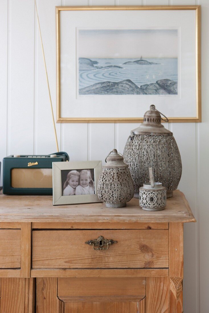 Set of three lanterns and photo on wooden sideboard against white, wood-clad wall