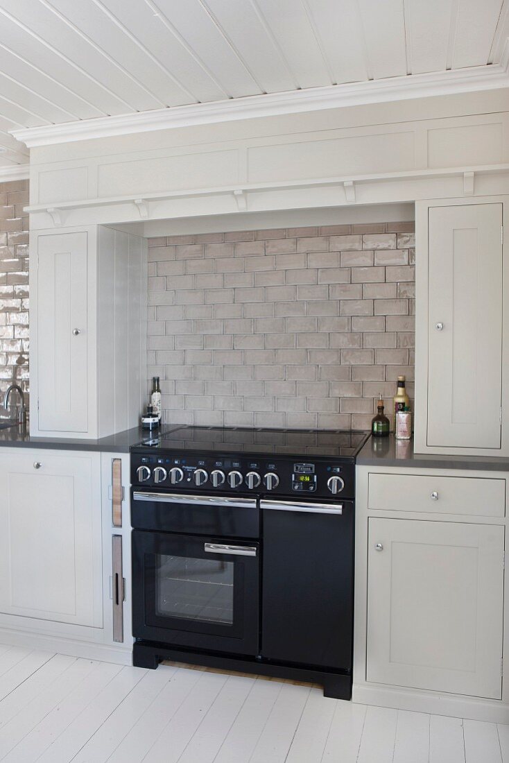 Black cooker in niche between pale grey fitted cupboards with pale grey tiles