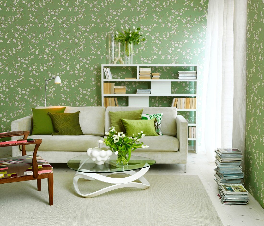 Couchtisch vor hellem Sofa mit Kissen vor Wand mit Tapete, helles Blumenmuster auf grünem Untergrund