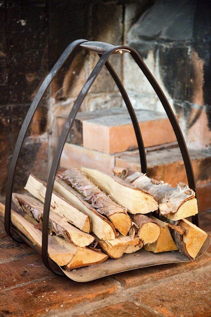 Firewood in curved metal rack in rustic fireplace