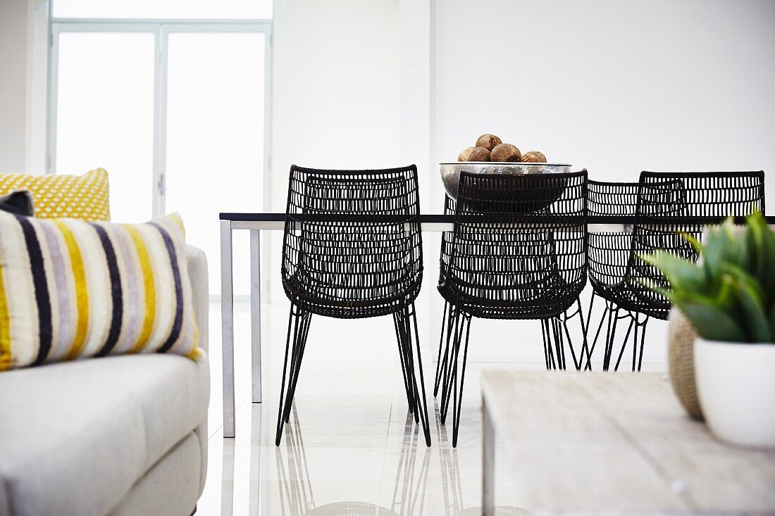 Blick von Loungebereich auf Essplatz mit dunklen Geflecht Stühlen um minimalistischem Tisch