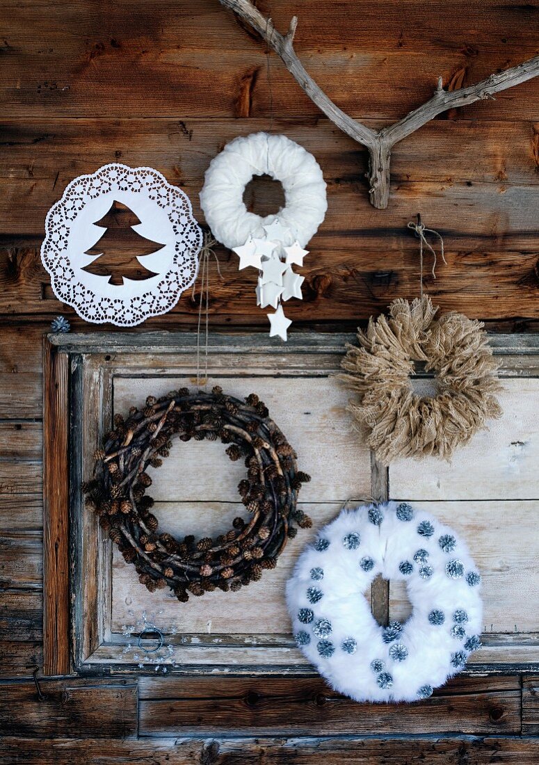 Selbstgemachte Dekokränze aus verschiedenen Materialien zu Weihnachten an rustikaler Holzhütte