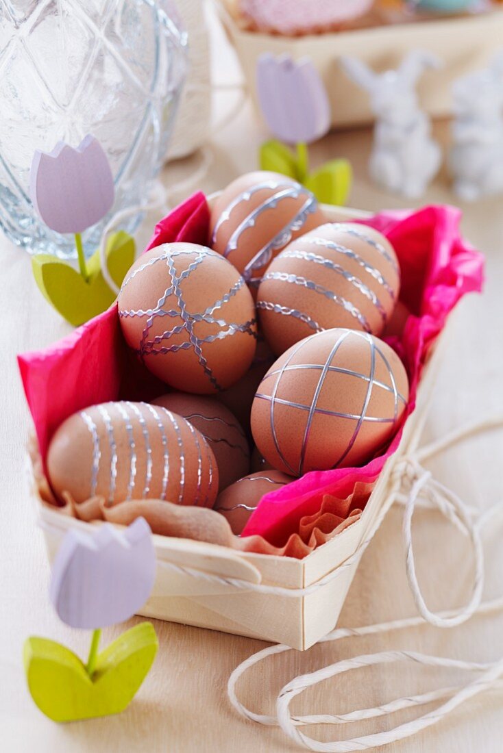 Braune Eier in Spankörbchen streifenmusterartig dekoriert mit silberfarbenen Aufklebern