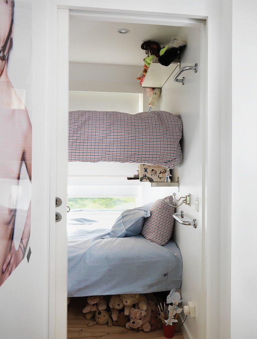 Blick in winziges Kinderzimmer mit in der Wand verankerten Stockbetten vor dem Fenster; Kuscheltiersammlung unterm Bett