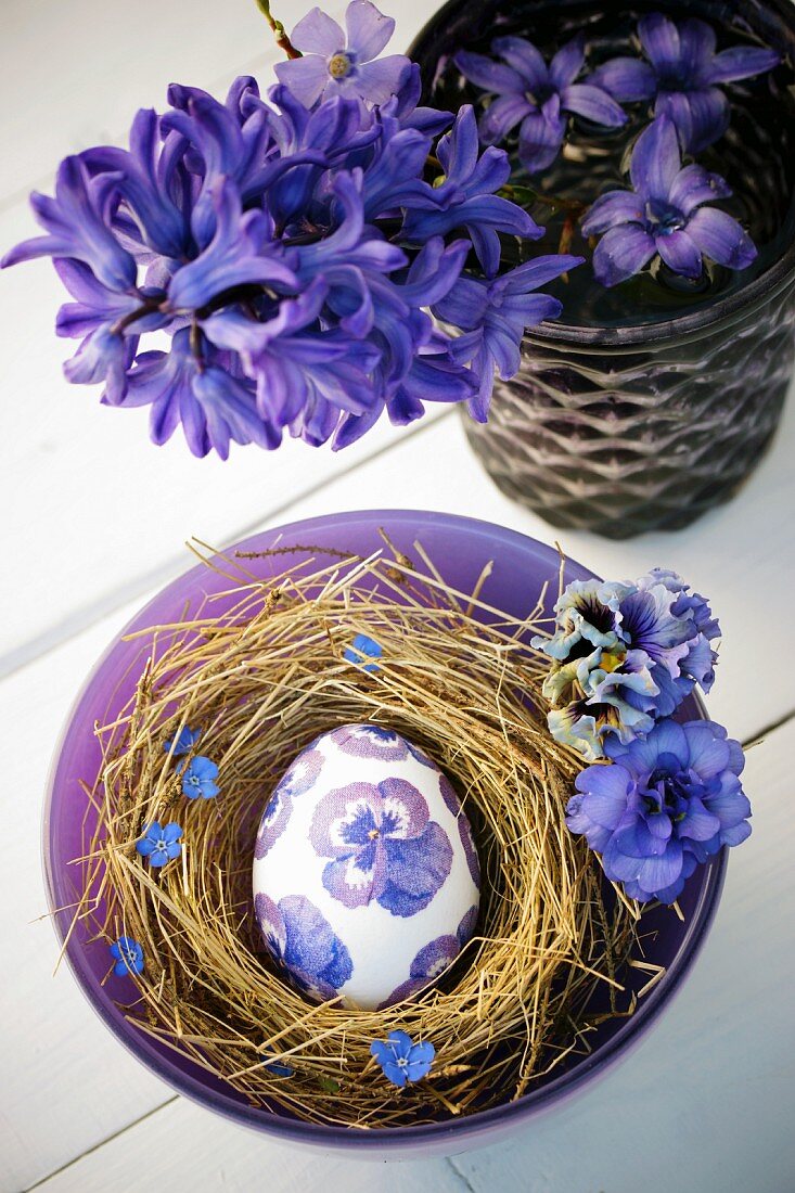 Osterei im Nest mit blauen Hornveilchenblüten in Serviettentechnik dekoriert
