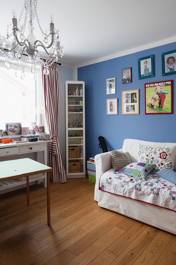 Ausziehbarer Sessel mit Kissen vor blau getönter Wand mit gerahmten Bildern, Schreibtisch am Fenster