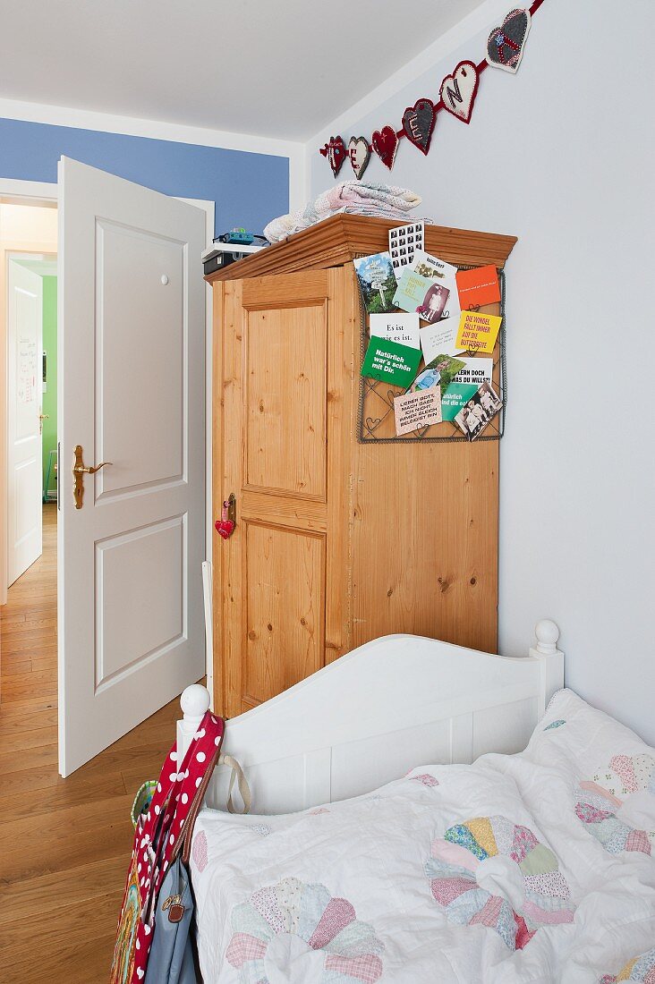 Bed with white wooden frame in front of farmhouse wardrobe in child's bedroom