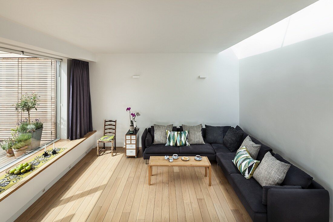 Eckcouch mit grauem Stoffbezug in minimalistischer Wohnraum mit Dielenboden und Panoramafenster mit eingebauter Bank