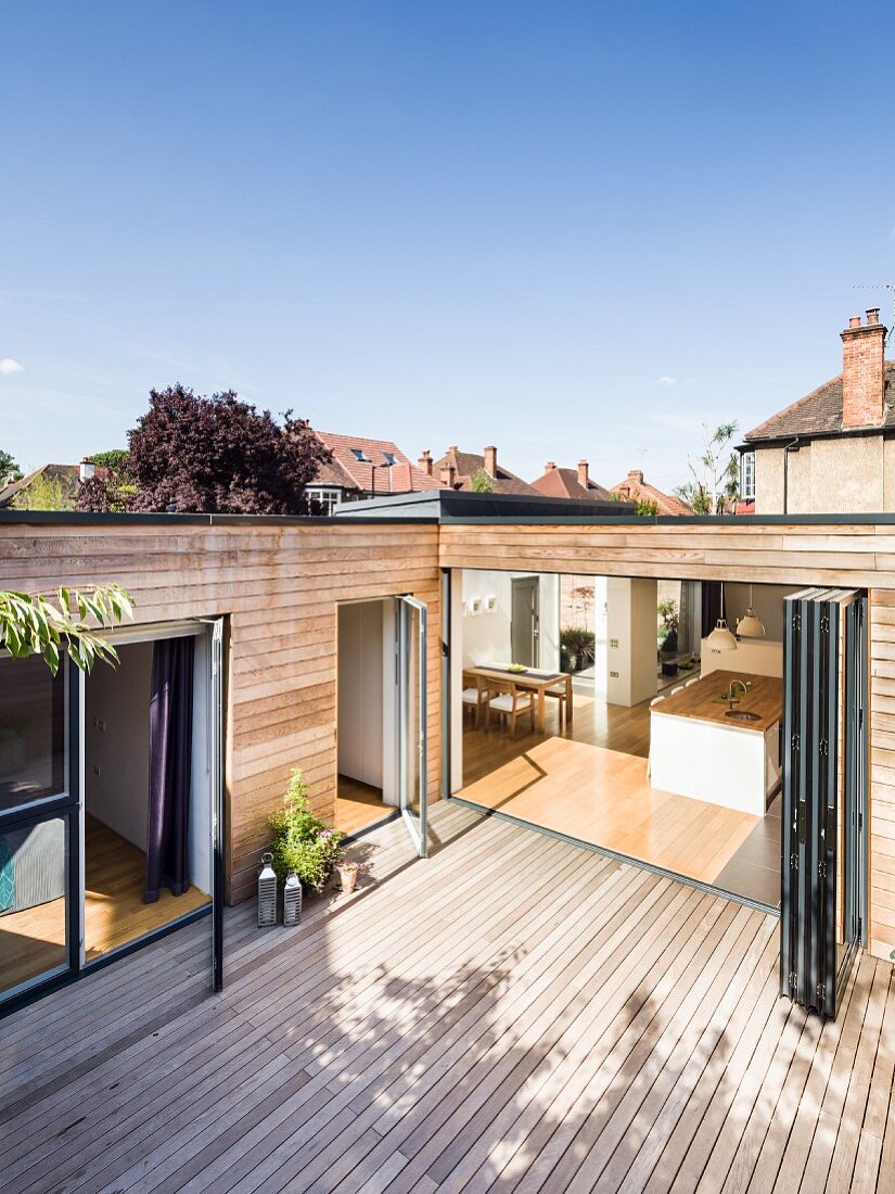 Wooden terrace of contemporary house with wood-clad facade; view into kitchen through open folding doors