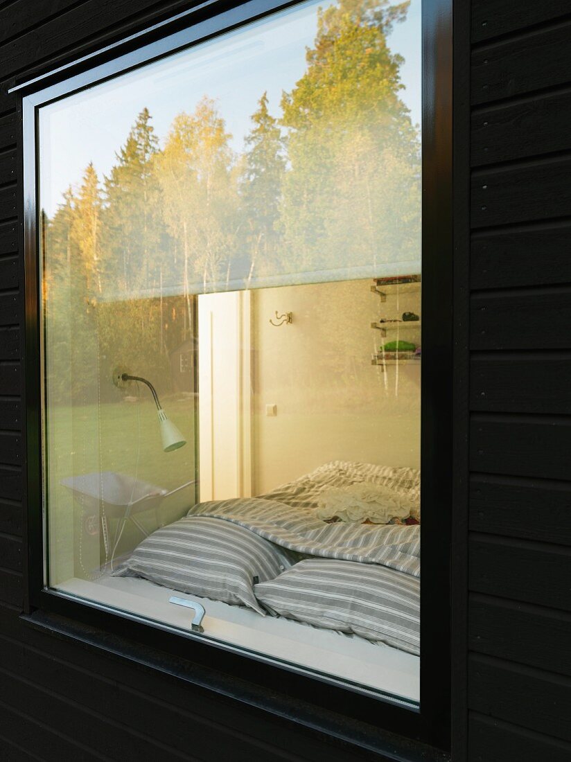 Swedish wooden house; trees reflected in bedroom window and view of bed