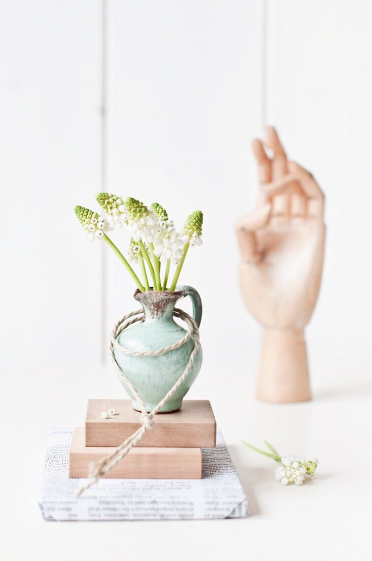 White muscari in pale green stoneware vase in front of sculpture of hand