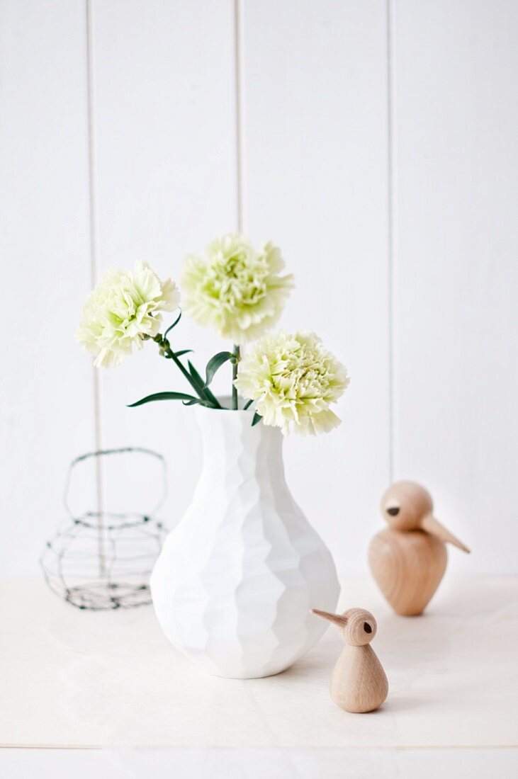 Grüne Nelke in moderner, weißer Vase mit kleinen Voegeln