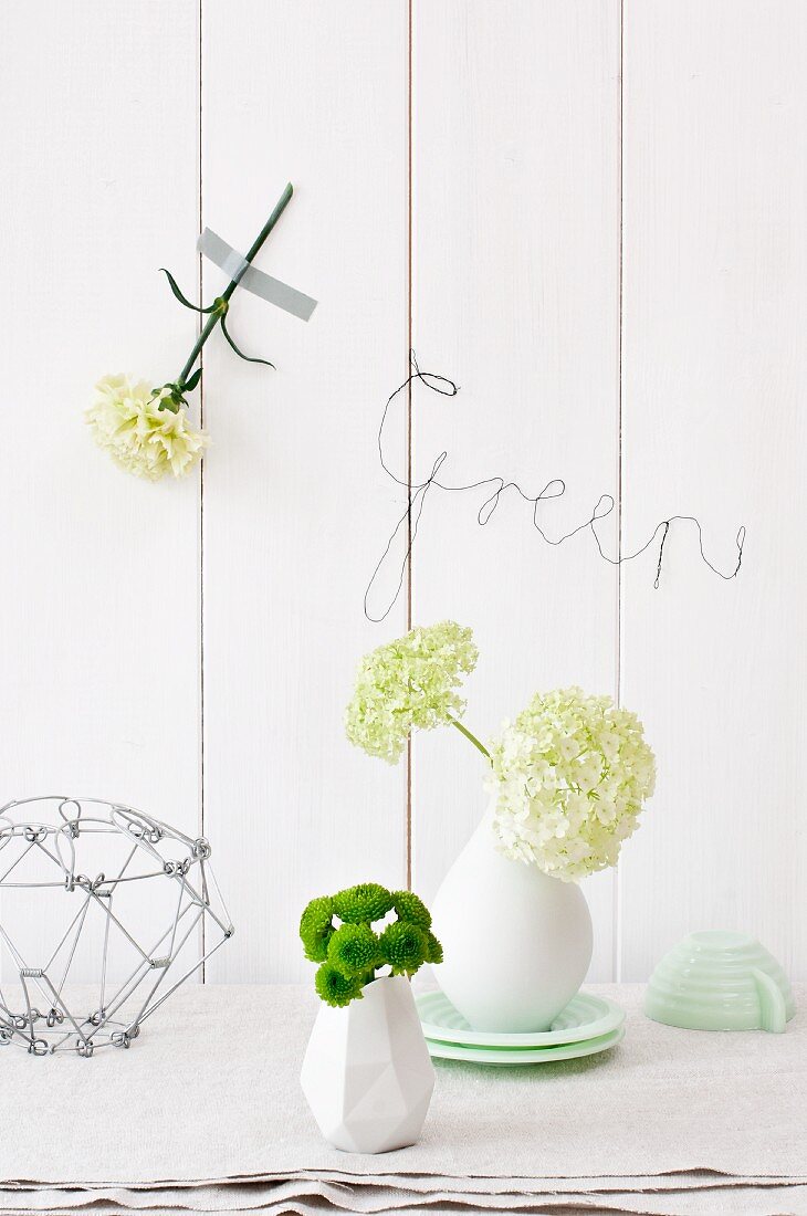 Small chrysanthemums and viburnum in vases, sweet William taped to wall and bent wire spelling 'Green'
