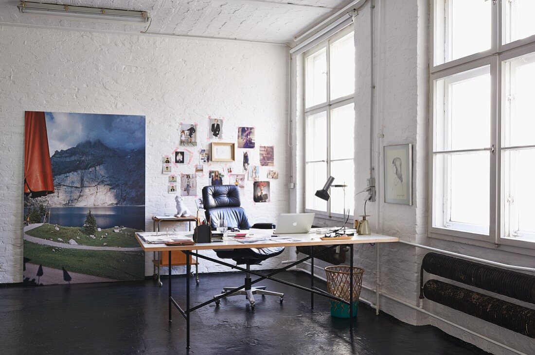 Eiermann-Tisch und Chefsessel in einer Loftwohnung; Landschaftsfoto und Moodboard im Hintergrund