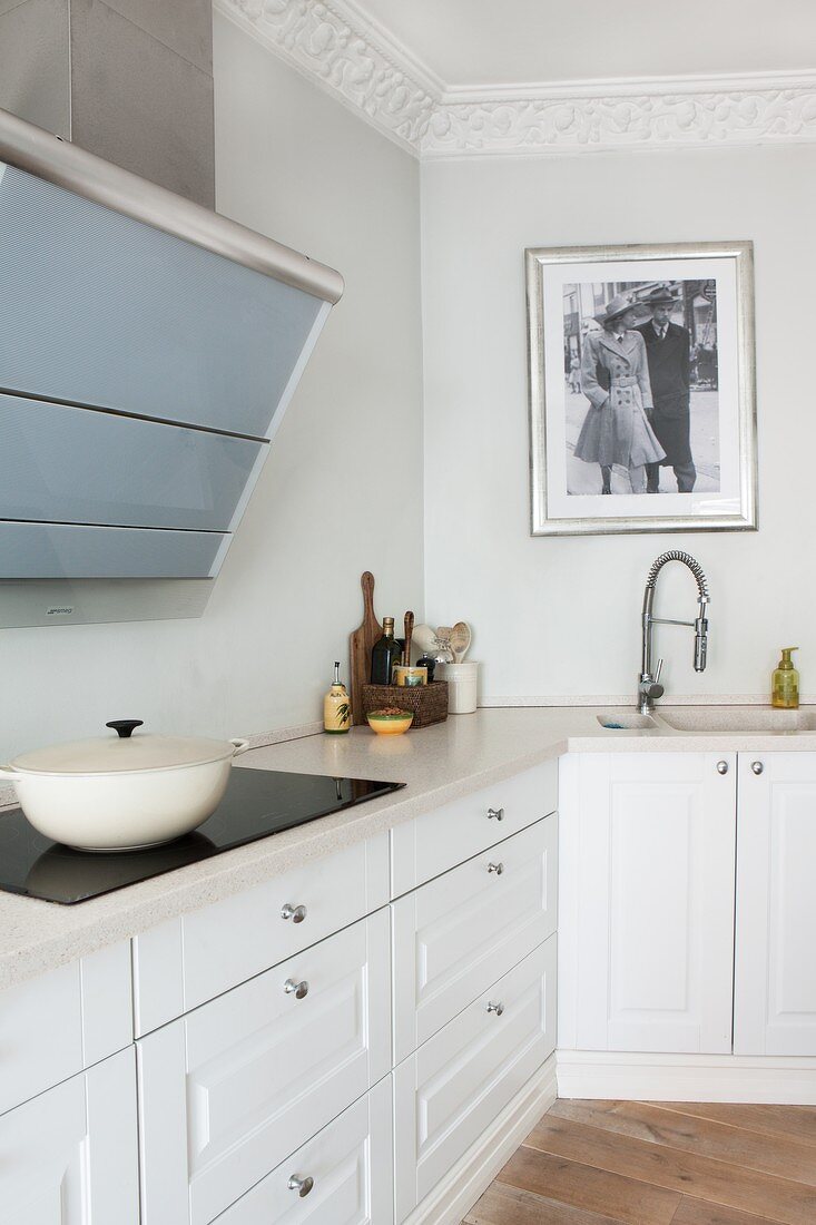 White fitted kitchen in period apartment with stucco frieze; cast iron pot on ceramic hob and historical black and white photo over sink