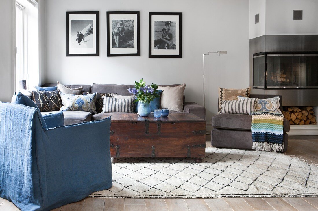 Sofa set, trunk table and blue, loose-covered armchair next to modern fireplace and black and white, framed family photos on wall
