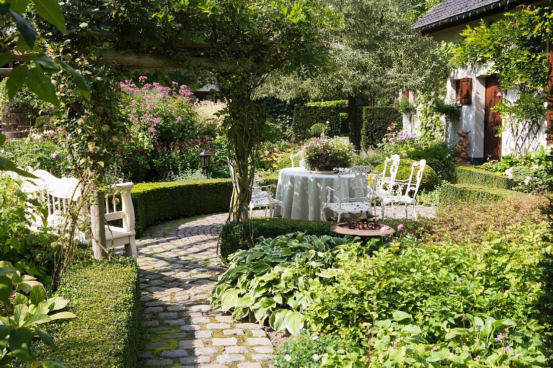 Angelegter Garten mit sonnigem Sitzplatz, im Hintergrund Wohnhaus