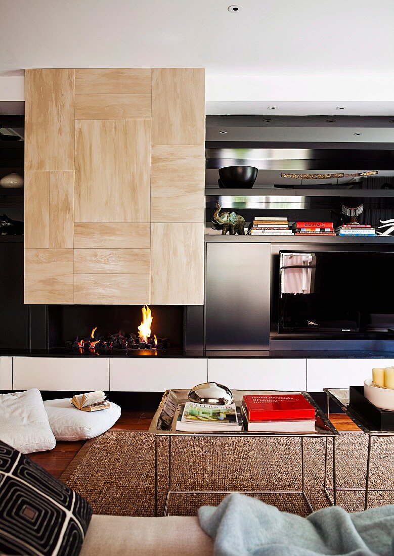 Loungebereich mit filigranen Beistelltischen vor modernem Wandschrank und integrierter, offener Kamin mit Feuer