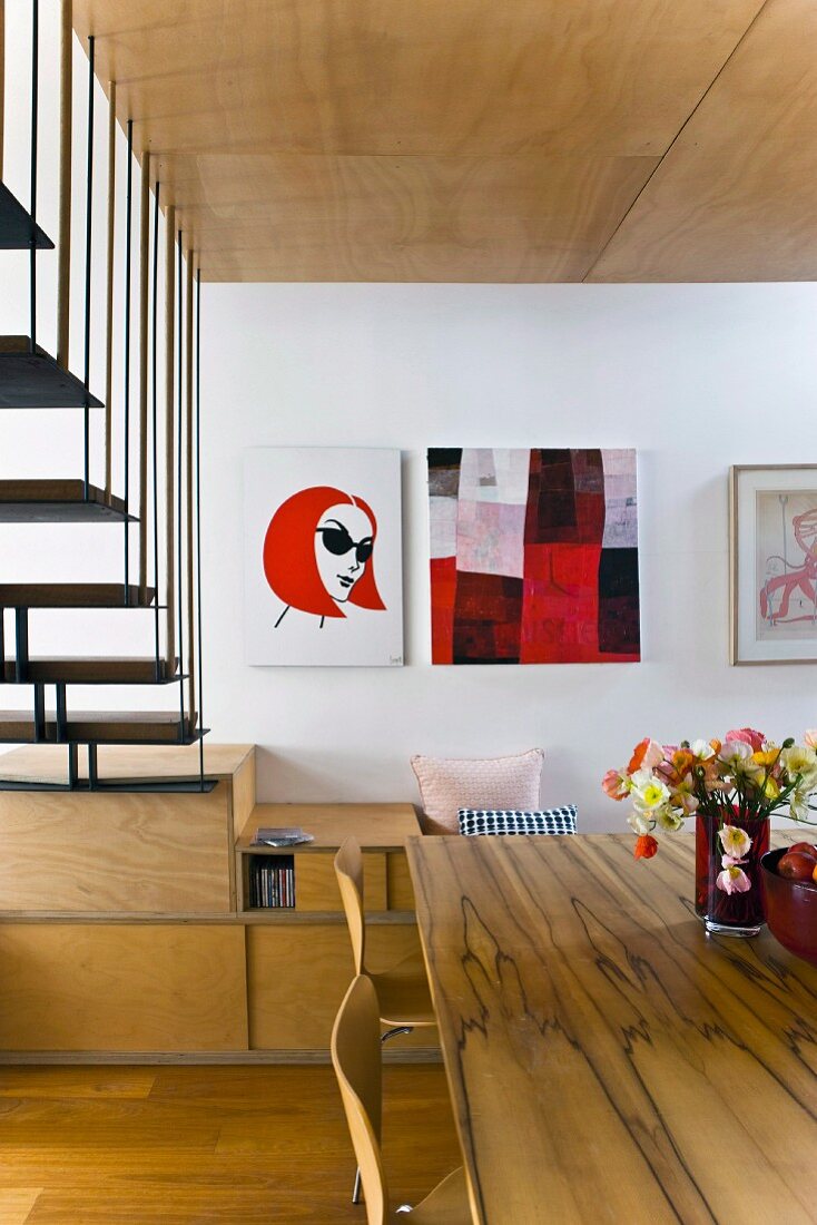 Esstisch aus Kiefernholz neben schwarzer Metalltreppe mit Podest aus Holz, an Wand moderne Bilder