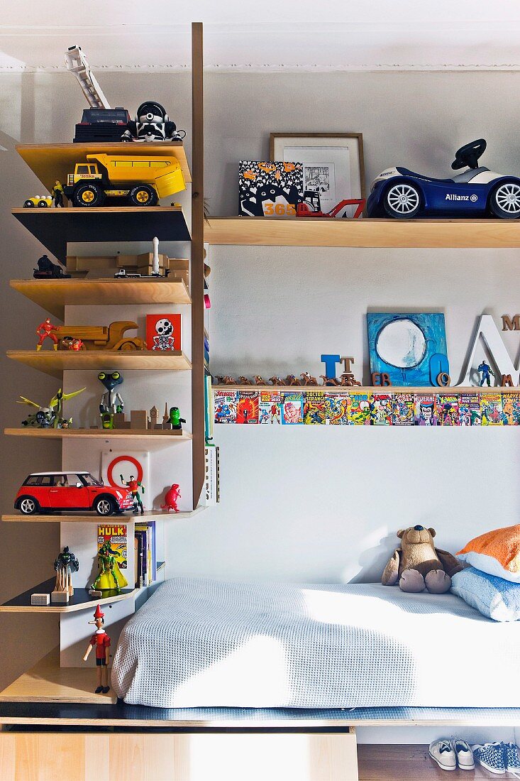 Regalböden übereck an Wand mit Spielsachen, teilweise sichtbare Matratze auf Holz Unterbau im Kinderzimmer