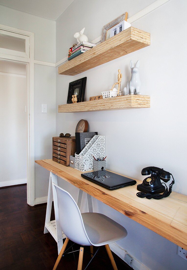 Untreated wooden shelves above wooden desk in home office with vintage telephone and classic chair