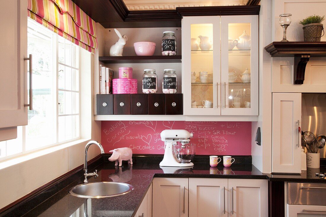 Black and white fitted kitchen with striped Roman blind and pink blackboard splashback
